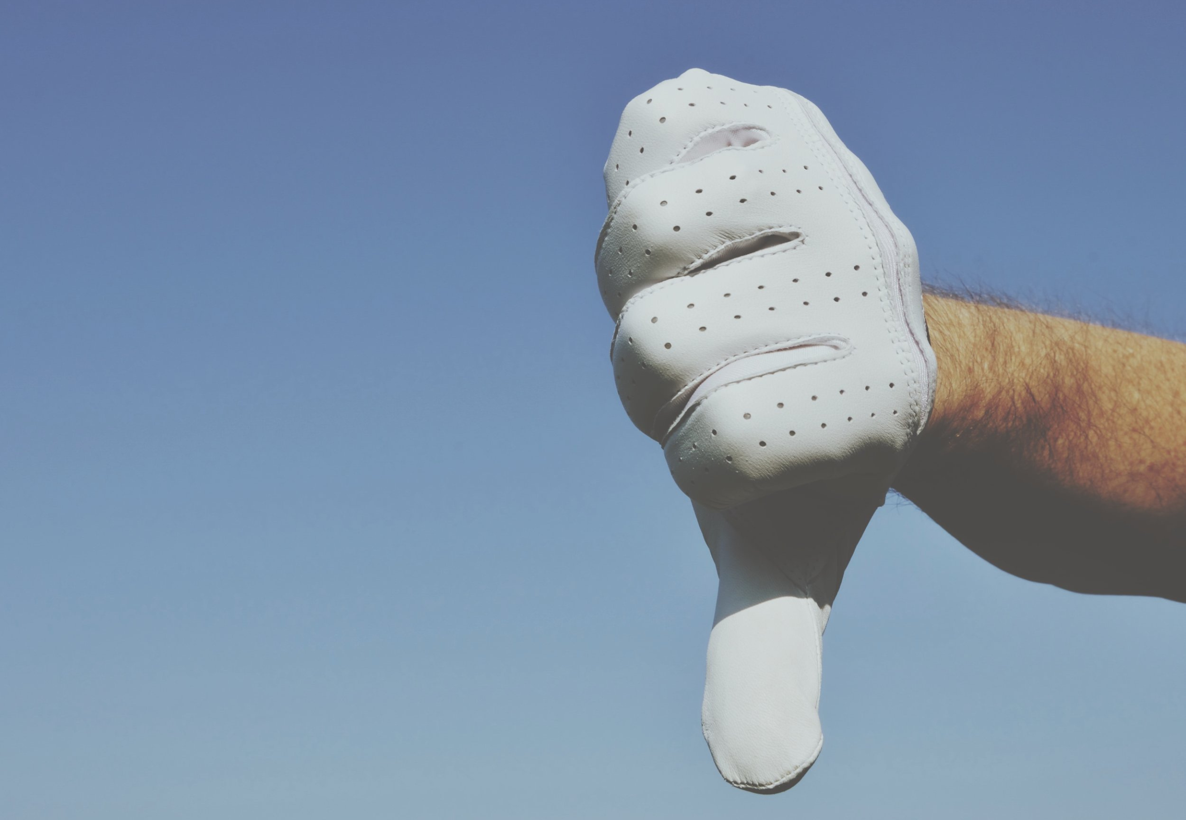 A golfer with a golf glove is pointing his thumb down.